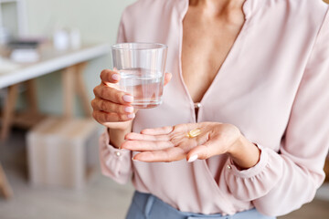 Close up of unrecognizable young woman holding vitamin capsule in hand with glass of water