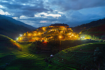 Aerial top view of hotel or houses with fresh paddy rice, green agricultural fields in countryside or rural area of Mu Cang Chai, mountain hills valley in Asia, Vietnam. Nature landscape background.