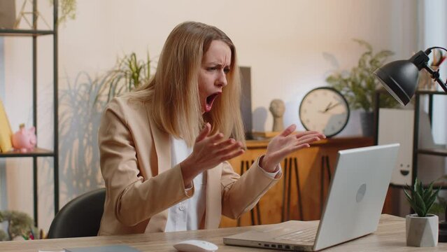 Young businesswoman programmer software developer fingers crossed working on laptop loses becoming surprised by bad news results fortune loss fail at home office. Deadline bankruptcy. Freelancer woman