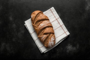 freshly baked bread on top of a tea towel on the black stone table, Stunning photo showing the crispy brown crust of freshly baked bread, resting on a soft kitchen towel and black stone surface