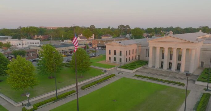 Aerial: Drone Panning Shot Of Us Flag Outside Federal Courthouse In Residential City During Sunset - Tuscaloosa, Alabama