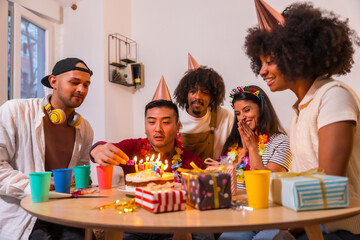 Multi-ethnic group of friends at a birthday party on the sofa at home with a cake and gifts,...