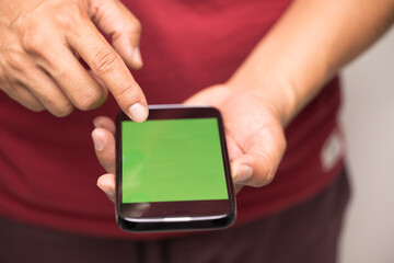 Closeup of men's hands holding cell telephone and green screen with blank copy space for your advertising text message or promotional conten.Red shirt man watching video on mobile smart phone.