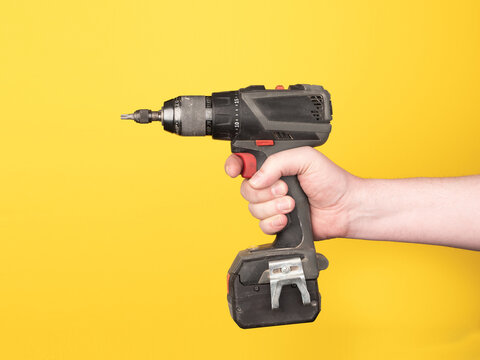 A hand holds a cordless screwdriver. No face, yellow background, copy space.
