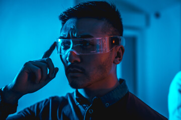Young chinese man with neon glasses with a blue light, futuristic concept, cyber human technology
