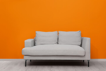 Comfortable sofa near bright orange wall indoors