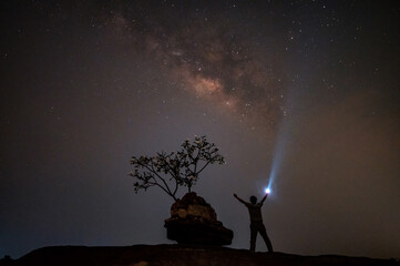 Man tourist with flashlight on the rock at night. Space background with noise and grain. Night...