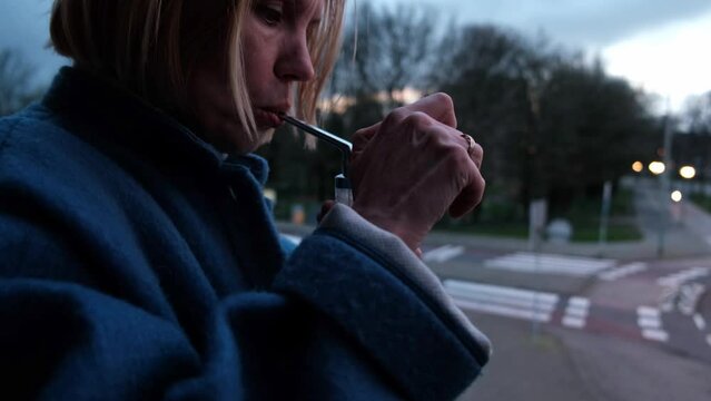 A woman smokes cannabis through a bong on the background of a city street.