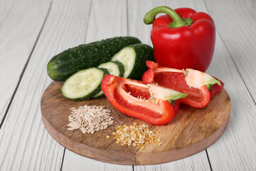 Fresh cucumbers, red bell peppers and vegetable seeds on white wooden table