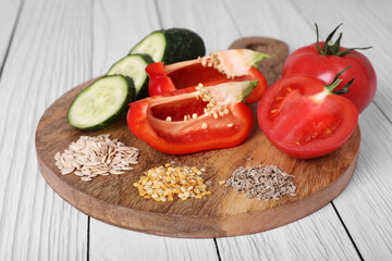 Fresh cucumbers, red bell peppers, tomatoes and vegetable seeds on white wooden table, closeup