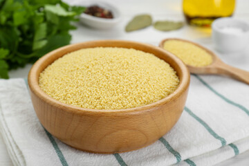 Bowl of raw couscous on white wooden table, closeup