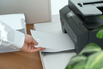Woman loading paper into printer at wooden table indoors, closeup