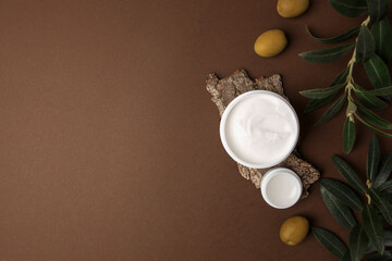 Obraz na płótnie Canvas Flat lay composition with jars of cream and olives on brown background. Space for text