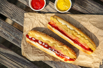 Fresh delicious hot dogs and sauces on wooden surface outdoors, flat lay