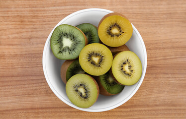 Bowl of many cut fresh kiwis on wooden table, top view