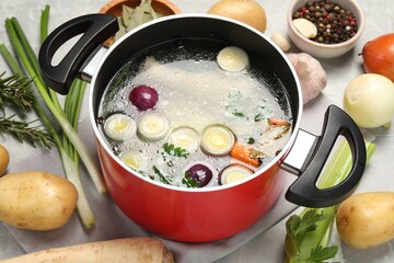 Pot with tasty bouillon and different ingredients on light grey table