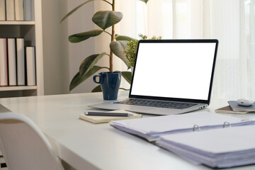 Laptop computer with blank screen, accountant documents, coffee cup and office supplies on white table.