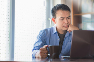 Asian man with coffee cup using laptop at home, Working from home concepts