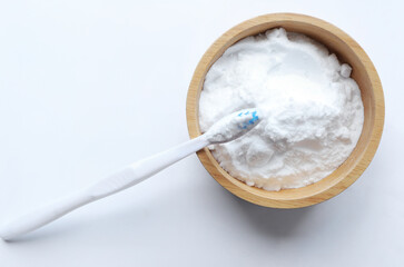 Close up of baking soda (sodium bicarbonate) in a wooden bowl with a toothbrush on white background. Teeth whitening concept.