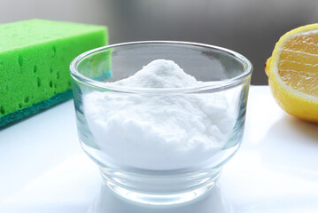 Baking soda (sodium bicarbonate) in bowl, lemon and sponge on the table. Home cleaning concept.
