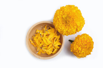 petals of fresh marigold in wooden bowl and yellow marigold flowers on white background. Top view. 