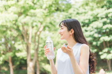 新緑の公園で散歩中に水分補給をする女性
