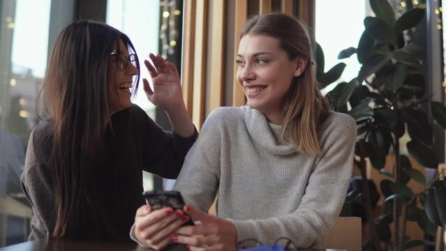 Gay female couple have postive expressions, sit close to each other at cafeteria, laughing joyfully. Lesbians couple and love concept