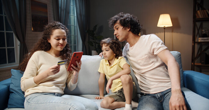 Asian family buys tickets for cheap flights on smartphone with credit card then funnily celebrates their upcoming adventure - happy family, travelling concept 