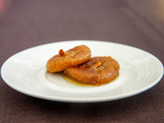 Dry fig dessert with sweet syrup as Turkish traditional sweet. Turkish name Incir Receli. Side view on white plate on wooden table.