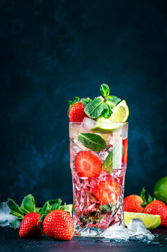 Strawberry Mojito cocktail drink with lime, white rum, soda, cane sugar, mint, and ice in glass on deep blue background. Summer refreshing beverage
