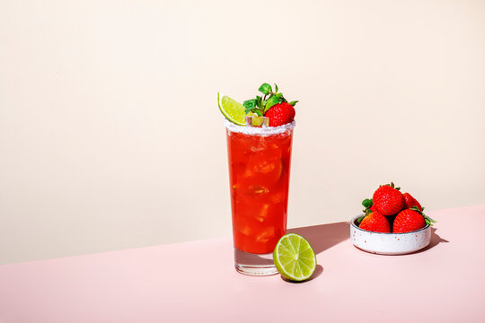Paloma alcoholic cocktail drink with tequila, grapefruit and lime juice, strawberries, mint and ice in glass with salty rim. Beige pink vanilla background.