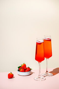 Rossini summer alcoholic cocktail drink with sparkling wine or prosecco, strawberry puree and ice in champagne glasses. Beige pink vanilla background, hard light, shadow pattern