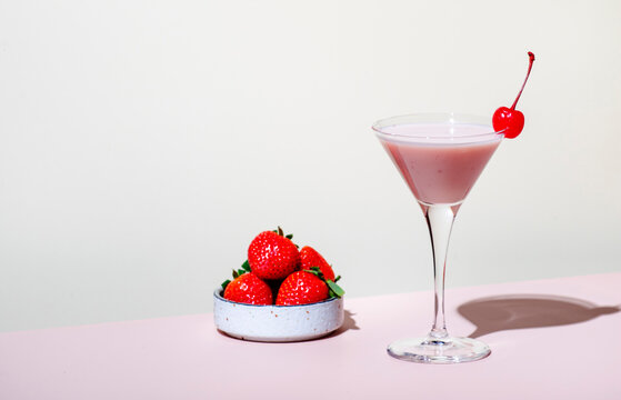 Bounty martini summer alcoholic cocktail drink with vodka, liqueur, cream, syrup, strawberries and ice in glass with cocktail cherry. Beige pink vanilla background