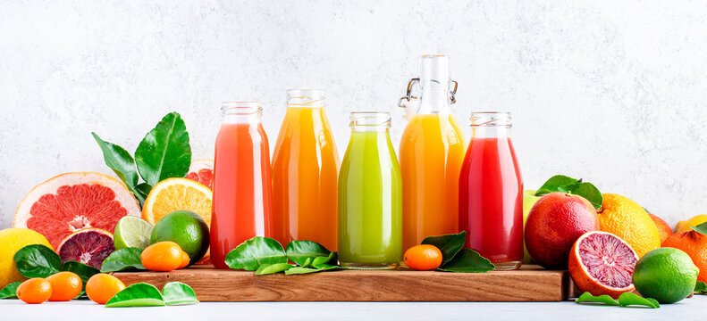 Summer beverages. Citrus fruit juices, fresh and smoothies, food background. Mix of different whole and cut fruits: orange, grapefruit, lime, tangerine with leaves and bottles with drinks, banner