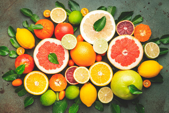 Citrus fruit food background, top view. Mix of different whole and sliced fruits: orange, grapefruit, lime and other with leaves on  green table