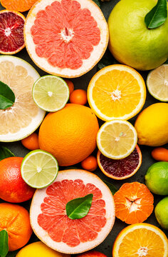 Citrus fruit food background, top view. Mix of different whole and sliced fruits: orange, grapefruit, lime and other with leaves on  green table
