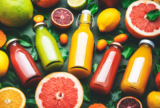 Summer drinks. Citrus fruit juices, fresh and smoothies, food background, top view. Mix of different whole and cut fruits: orange, grapefruit, lime, tangerine with leaves and bottles with drinks 