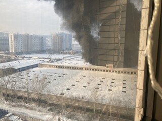 Large fire with black smoke. Burning industrial building, warehouse. A pillar of black smoke in the sky.