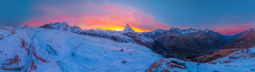 Naklejka na ściany i meble Aerial panorama view of Matterhorn mountain with amazing colorful twilight romantic sky in Switzerland. Wide establishing nature landscape sunrise or sunset of Zermatt travel ski resort in Swiss alps.