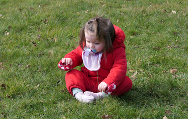 Small girl with a red coat having fun playing on grass in a garden on a sunny day