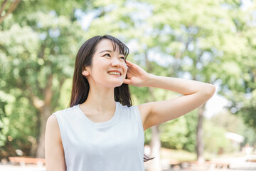 新緑の中で髪を触る笑顔の日本人女性（シャンプー・美髪）
