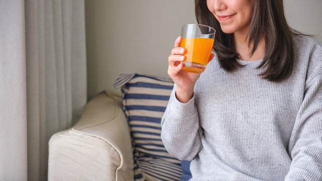 Closeup image of a young woman holding and drinking fresh orange juice at home