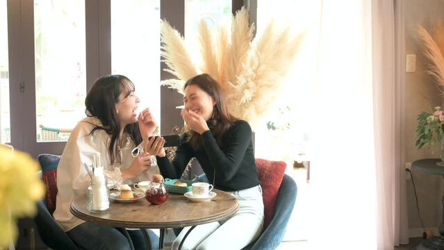 カフェでスマートフォンを見ながら談笑する女性客