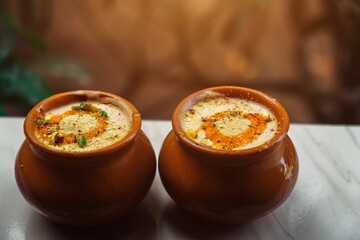 Kulfi or Qulfi ice cream in a clay pot. Kulfi is a popular traditional Indian dessert made of milk with spices and nuts. Two clay pots with ice cream on a blurry background - obrazy, fototapety, plakaty