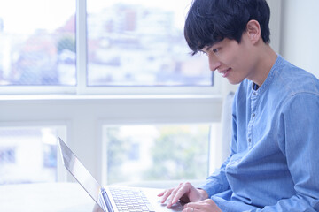 窓辺でノートパソコンを使う男性ビジネスパーソン
