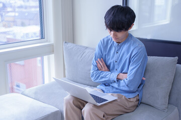 窓辺でパソコンを見て考える男性