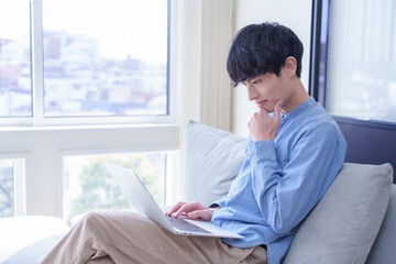 窓辺でパソコンを見て考える男性