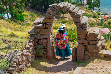 Peruvian indigenous Quechua women in traditional clothing walking on Isla Taquile, Titicaca Lake,...