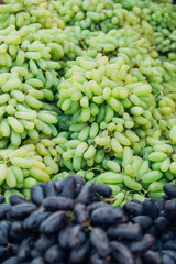 There are a lot of Green and black grapes on the market. Black and green fruit background. Raw materials for wine production