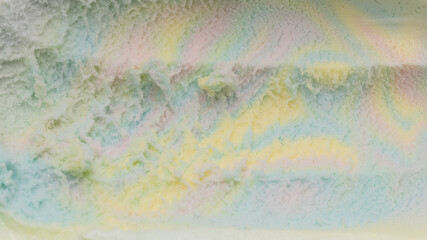 Close-up of rainbow-flavored ice cream scooped out of the container until it forms a groove.